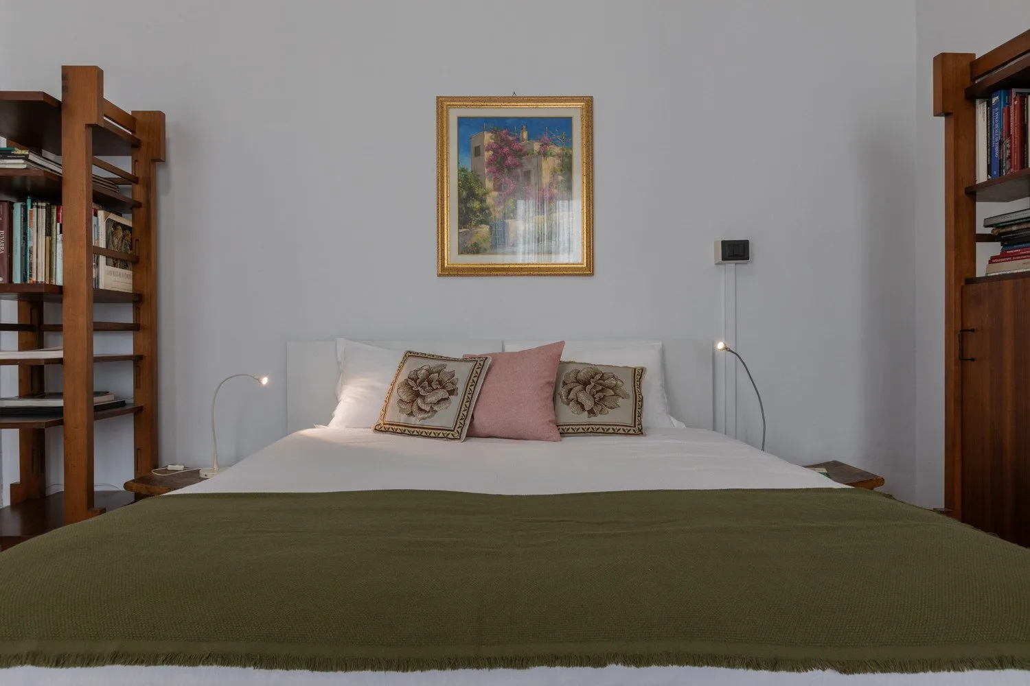 Un dormitorio con una cama bien tendida, una obra enmarcada y estanterías.