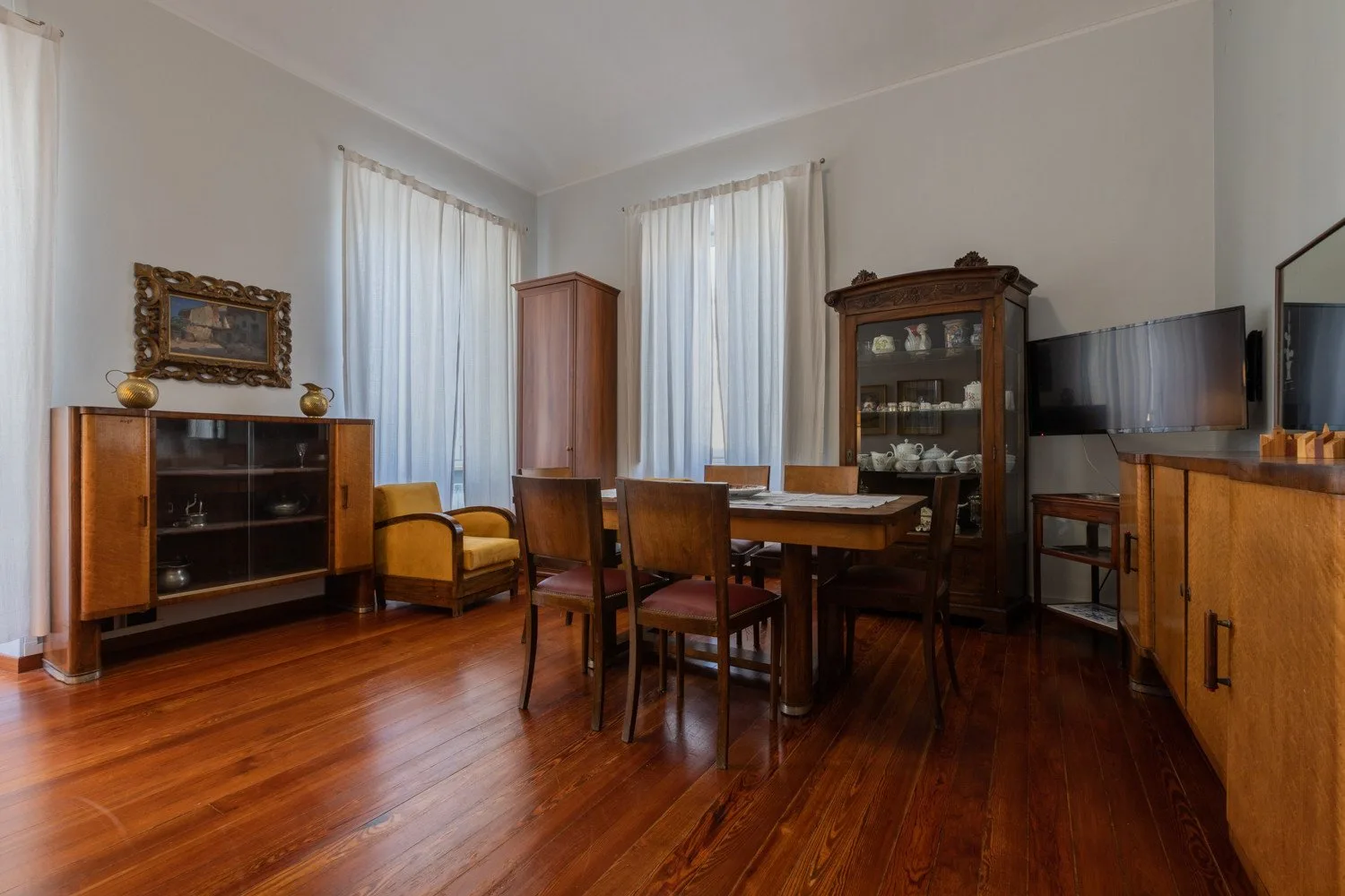 Un comedor con una mesa de madera y sillas junto a un aparador con puertas de cristal.
