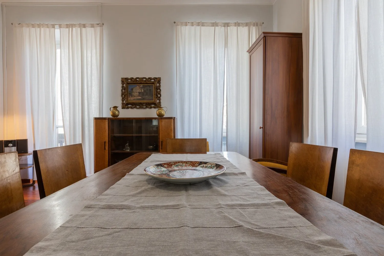 Un comedor con una mesa larga de madera y cortinas blancas.