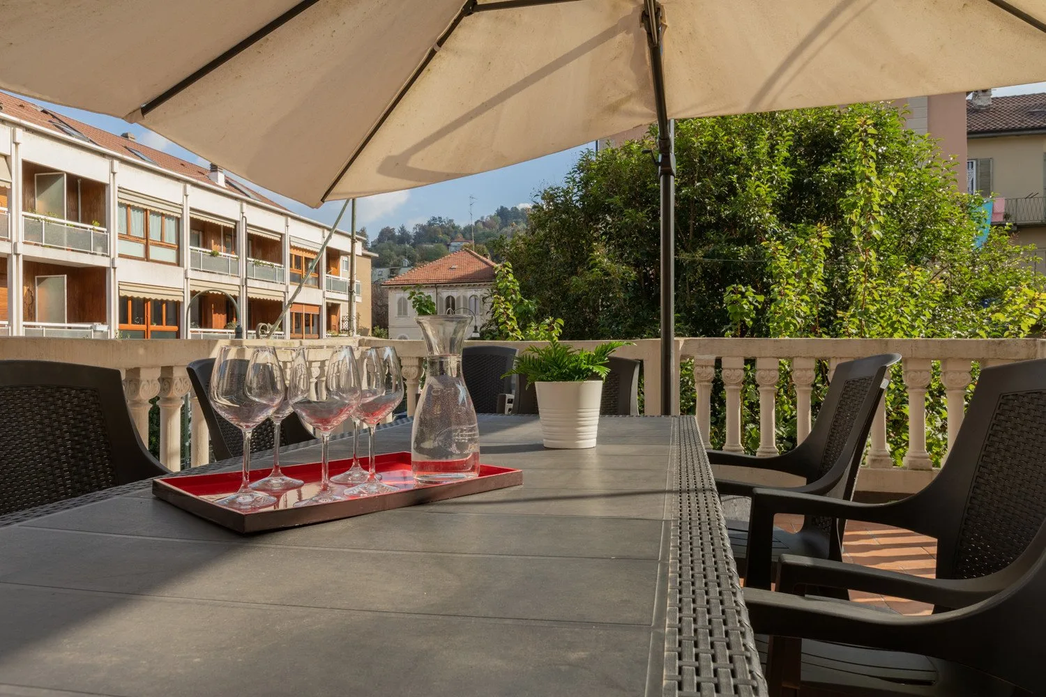 Una zona de comedor en una terraza al aire libre con mesa, asientos y una sombrilla grande.