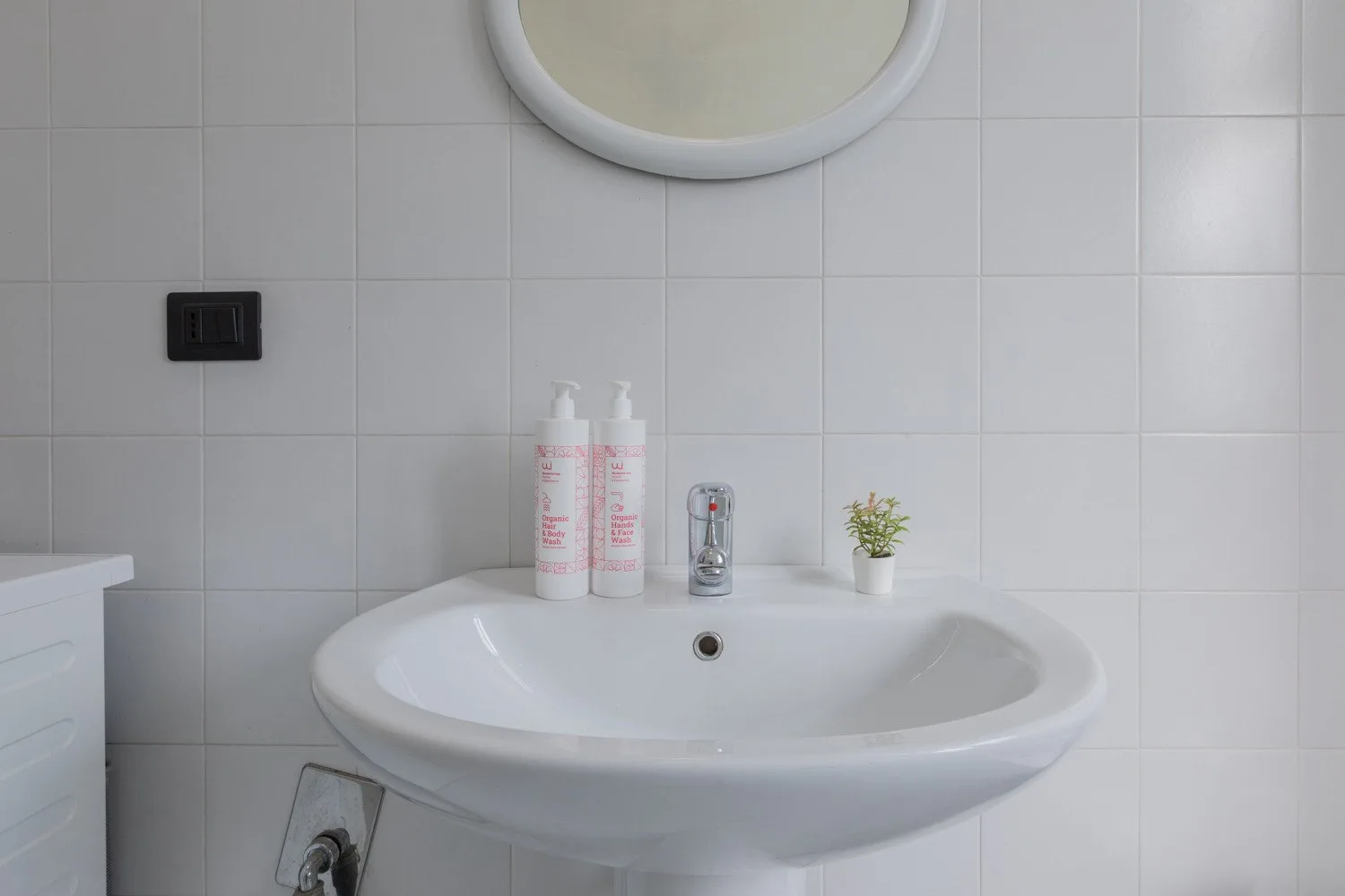 Un lavabo de baño está bajo un espejo redondo frente a una pared de azulejos.