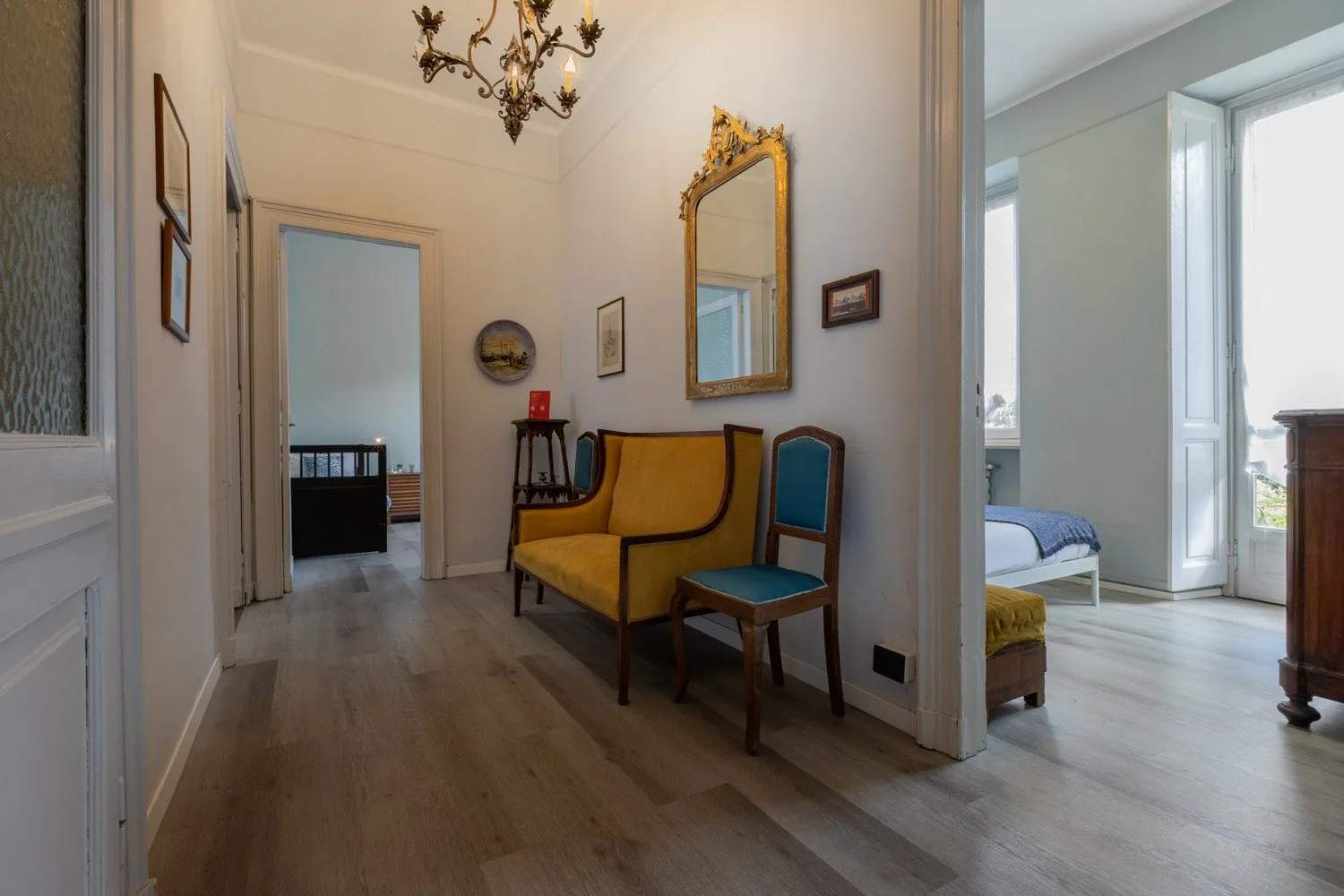 Un pasillo interior luminoso se abre a habitaciones contiguas, con asientos bajo un espejo.