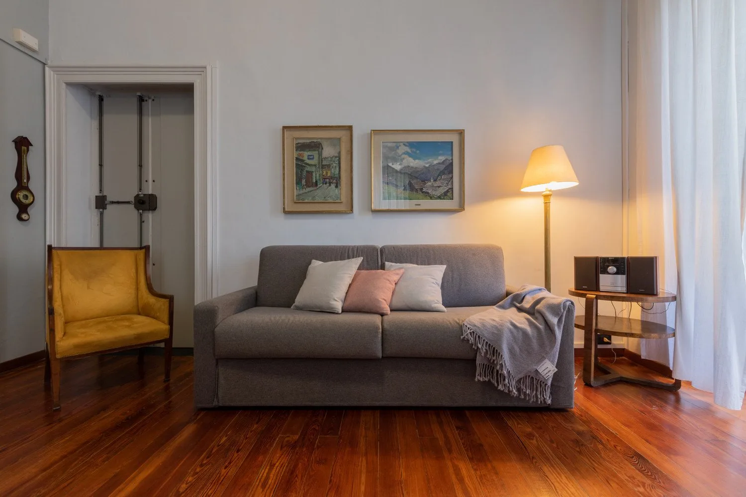 Una sala de estar con un sofá gris, cuadros enmarcados y una lámpara de pie encendida.
