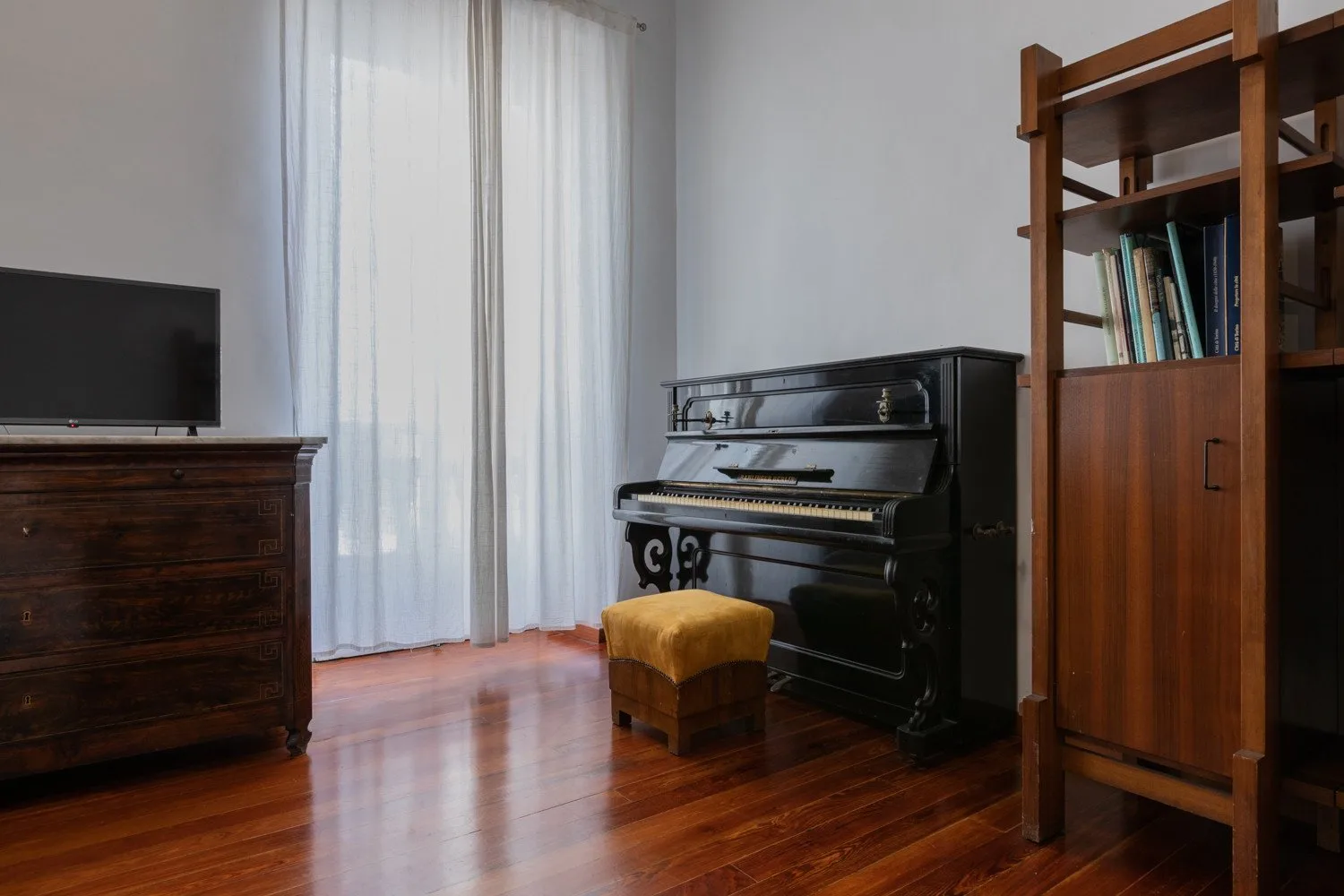 Una habitación con un piano vertical negro, estanterías de madera y suelo de madera pulida.