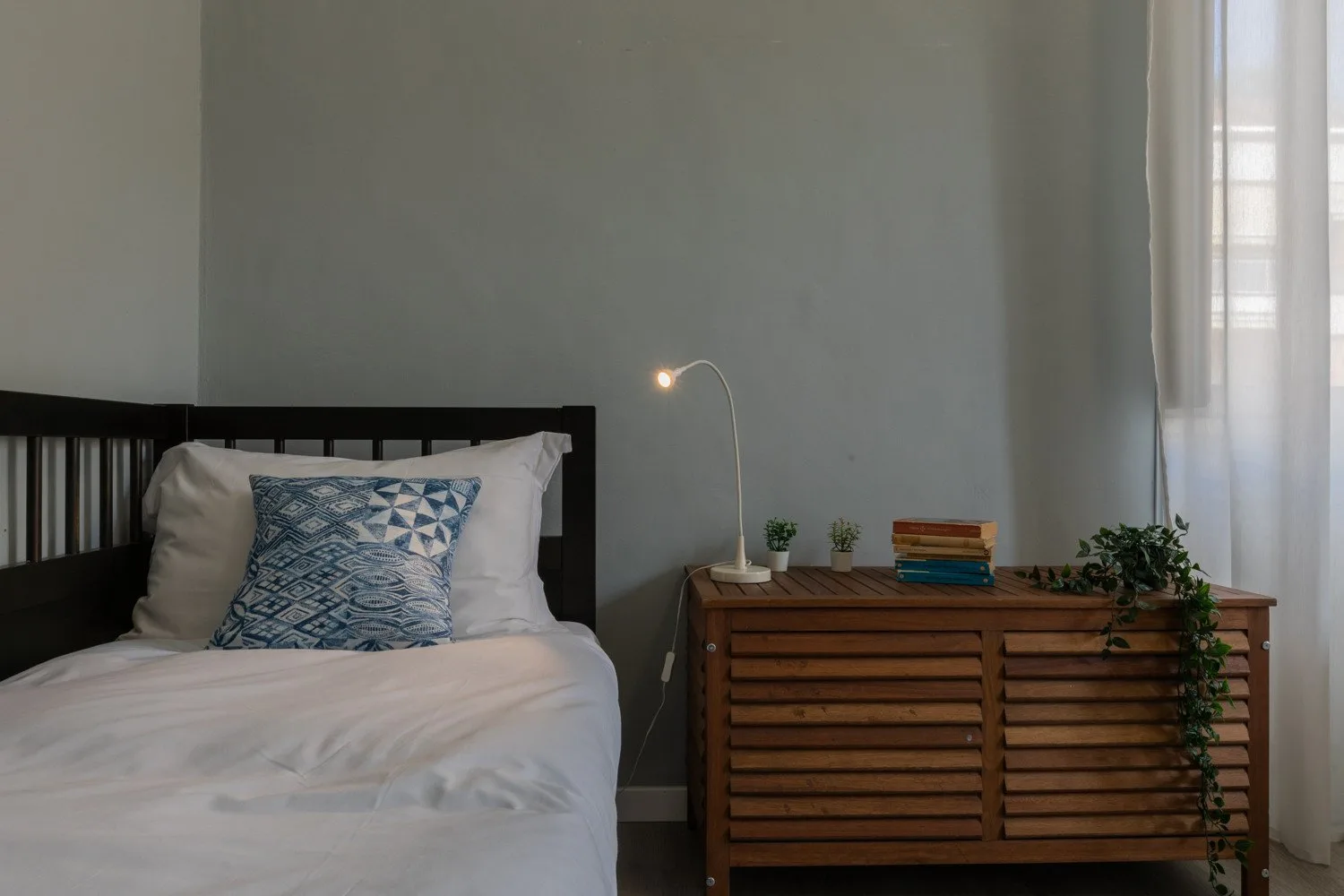 Un dormitorio con una cama junto a una cómoda de madera y una ventana con cortina.