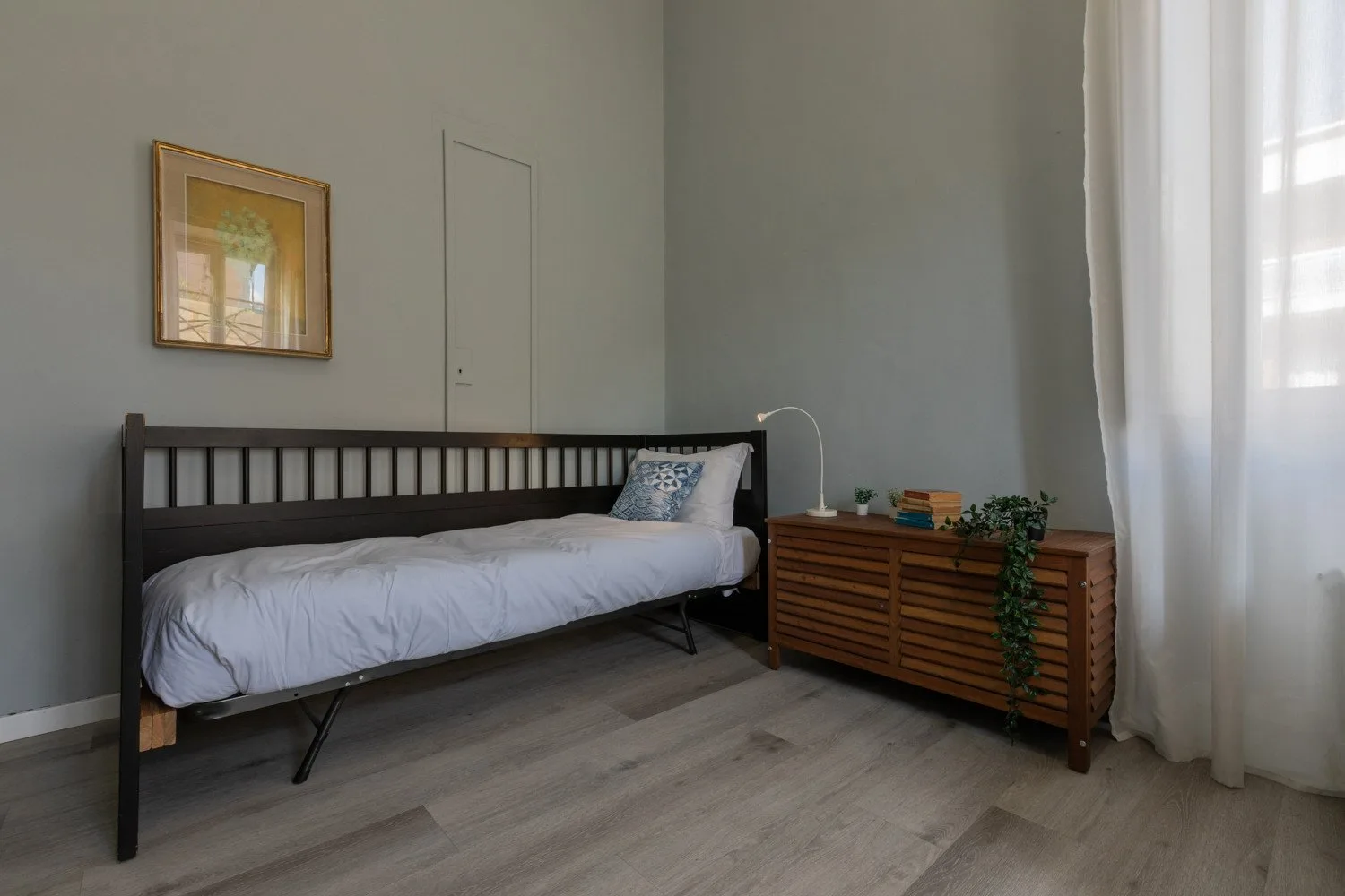Un dormitorio con una cama individual y una cómoda de madera junto a la ventana.