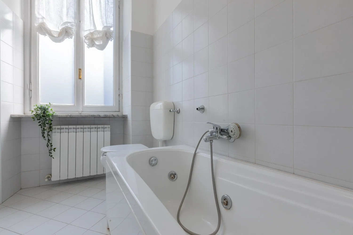 Un baño luminoso con azulejos y una bañera bajo una ventana.