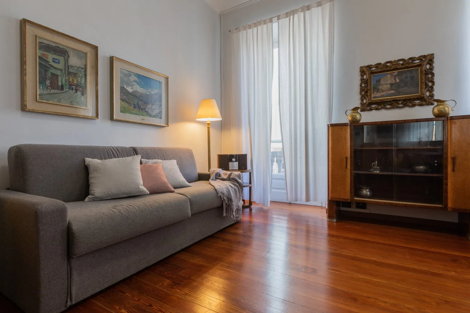 Una sala de estar con un sofá gris, cuadros enmarcados y un aparador.
