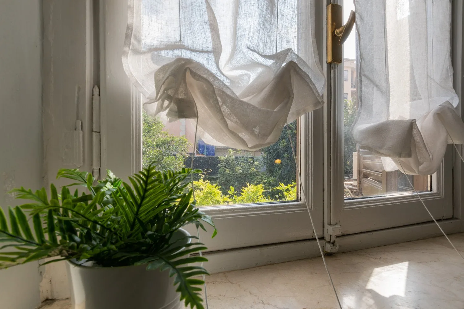 Una ventana luminosa con cortinas translúcidas da a la vegetación, con una planta frondosa en el alféizar.