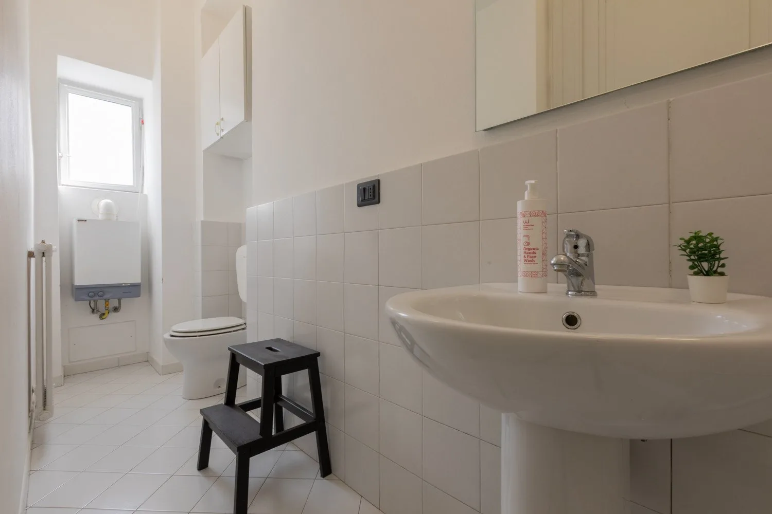 Un baño alicatado con lavabo, inodoro y un pequeño taburete.