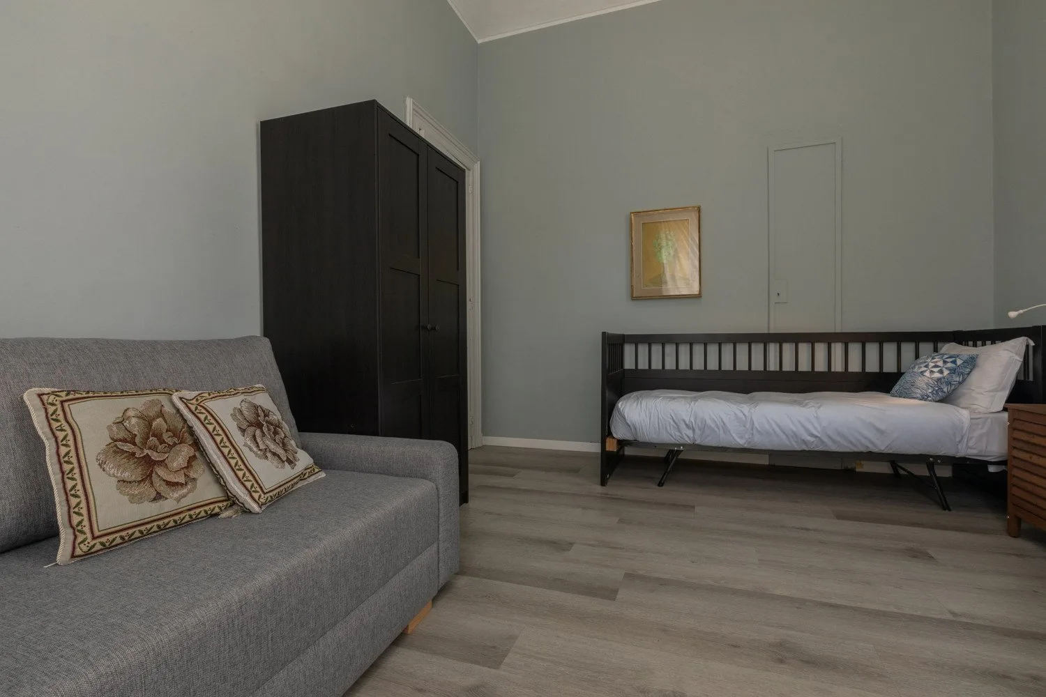 Un dormitorio con una cama, un sofá gris y un armario oscuro.