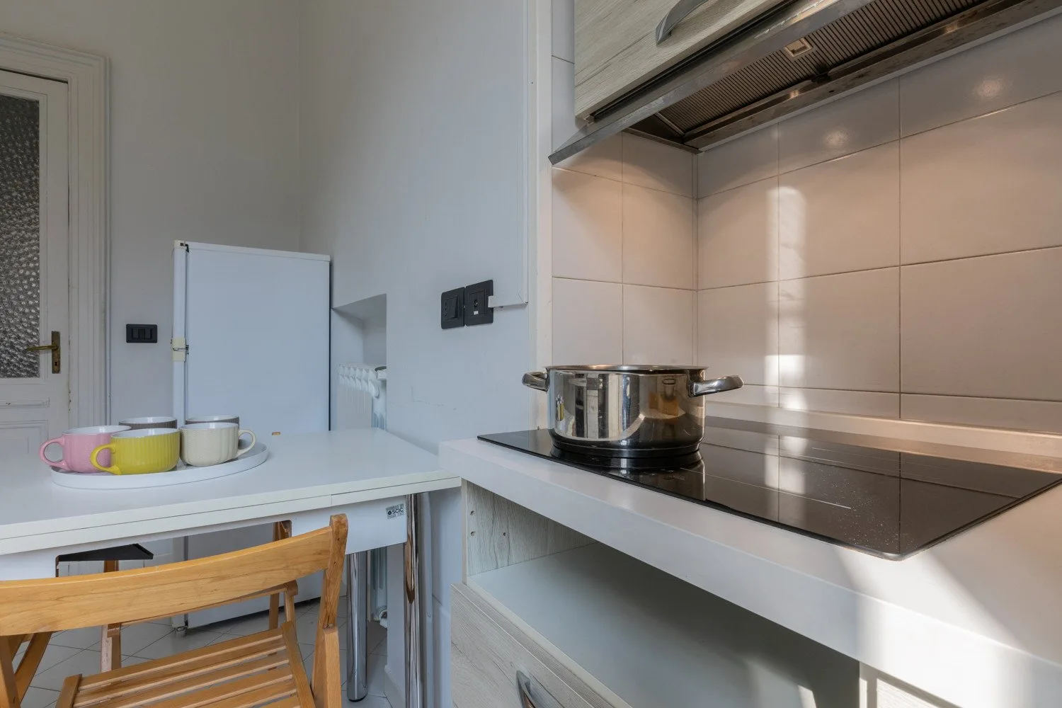 Una cocina pequeña con una placa de cocción y una mesa con tazas.