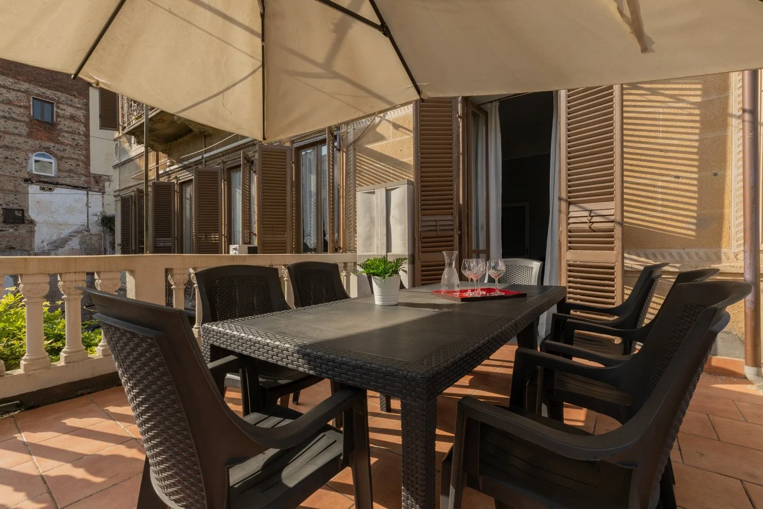 Una zona de comedor al aire libre con mesa y asientos junto a ventanas con contraventanas.