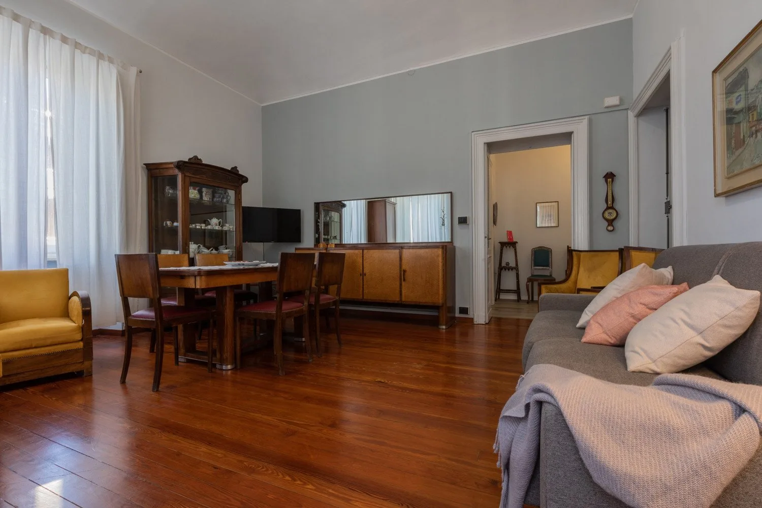 Una sala de estar con mesa de comedor, muebles de madera y un sofá gris.