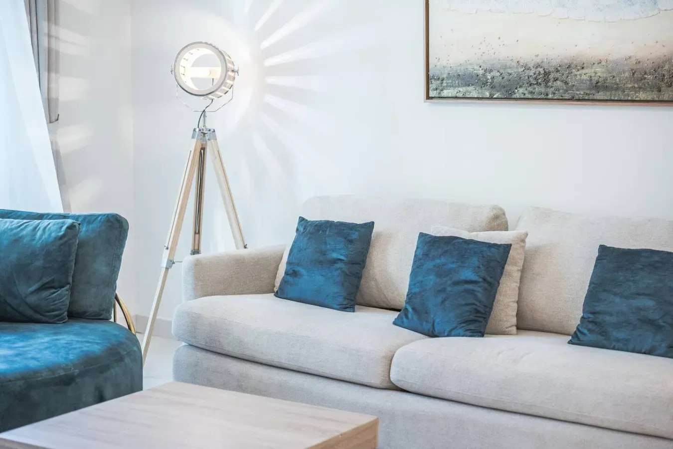 Una sala de estar con asientos claros y cojines azules junto a una lámpara de pie.