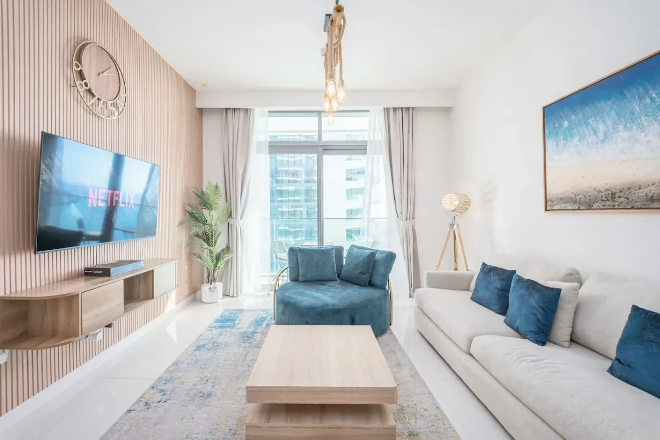 Una sala luminosa con asientos azules, un sofá claro y una ventana grande.