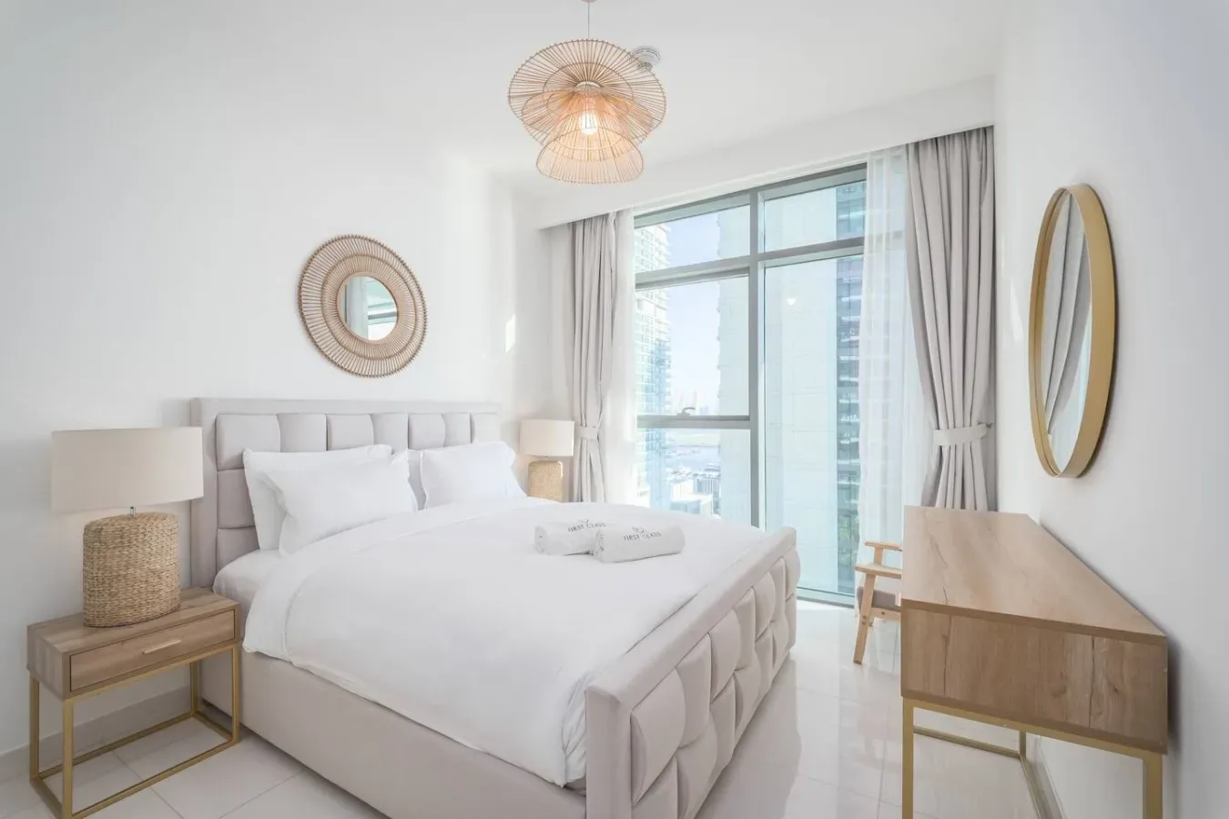 A bright bedroom with a large bed beside tall windows and light curtains.