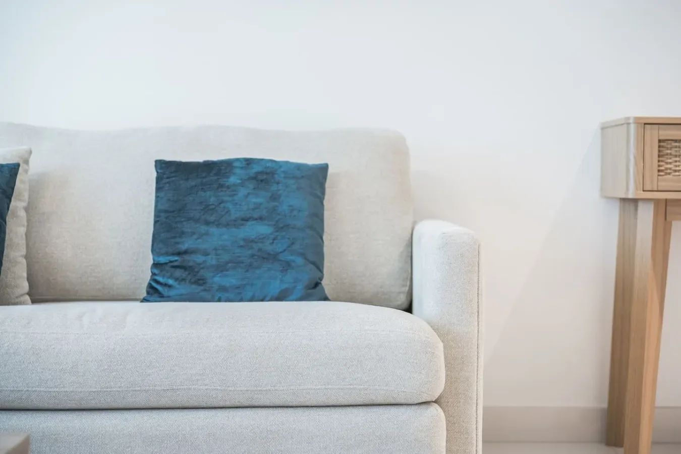 Un sofá de color claro con un cojín azul oscuro está junto a una mesa auxiliar de madera.