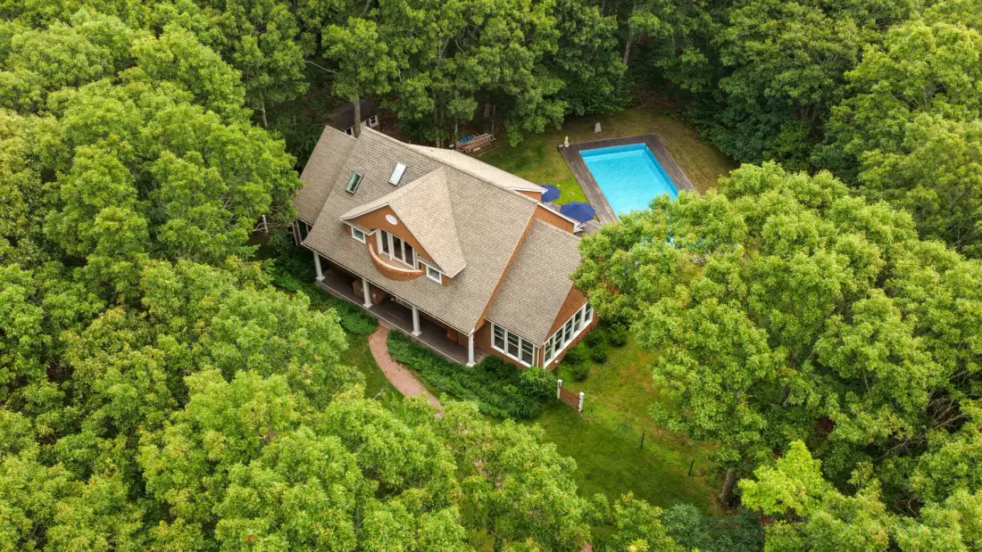 Vista aérea de una casa rodeada de árboles, con una piscina cerca.