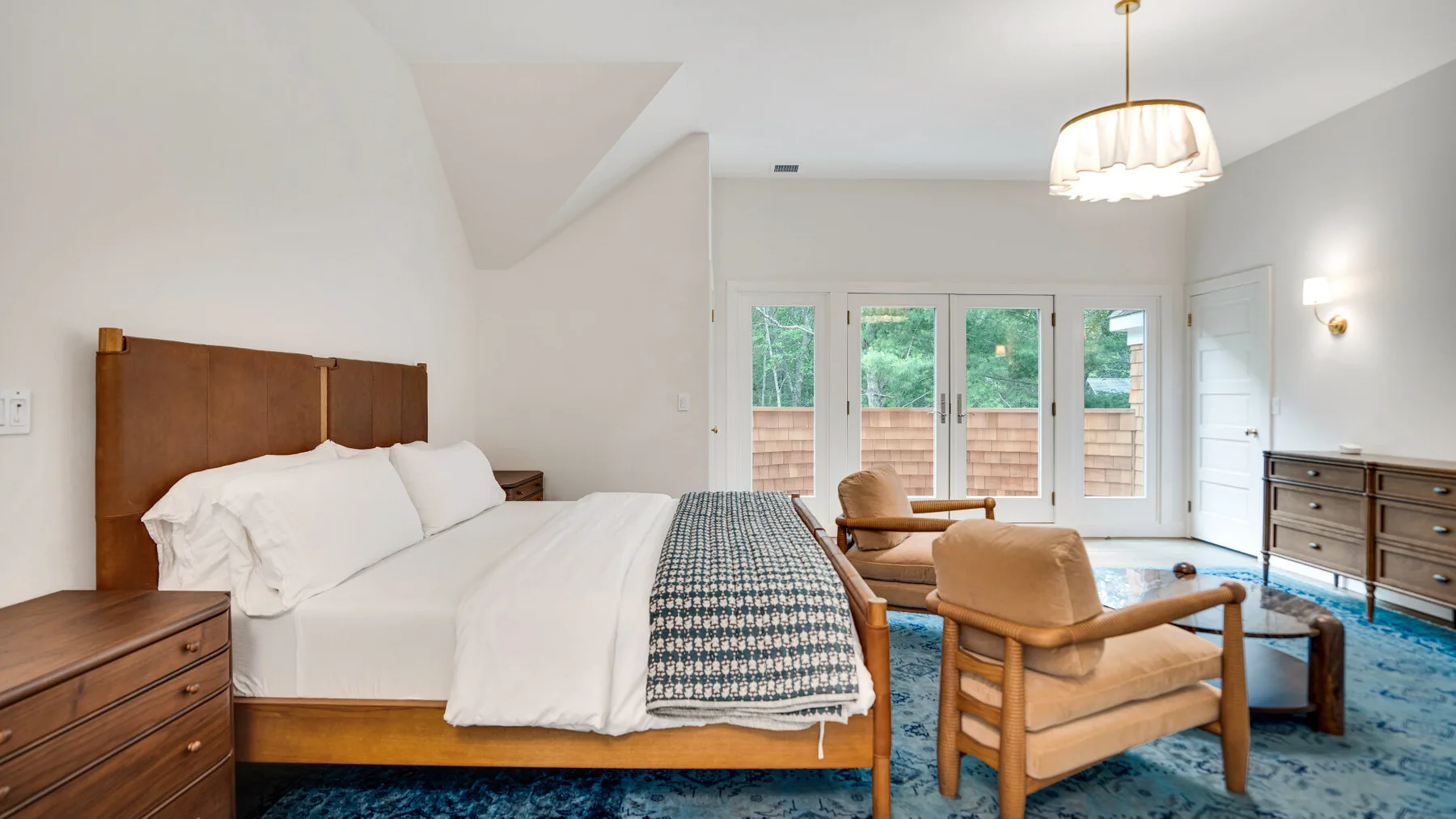 Un dormitorio luminoso con una cama de madera, ropa de cama blanca y asientos junto a las ventanas.
