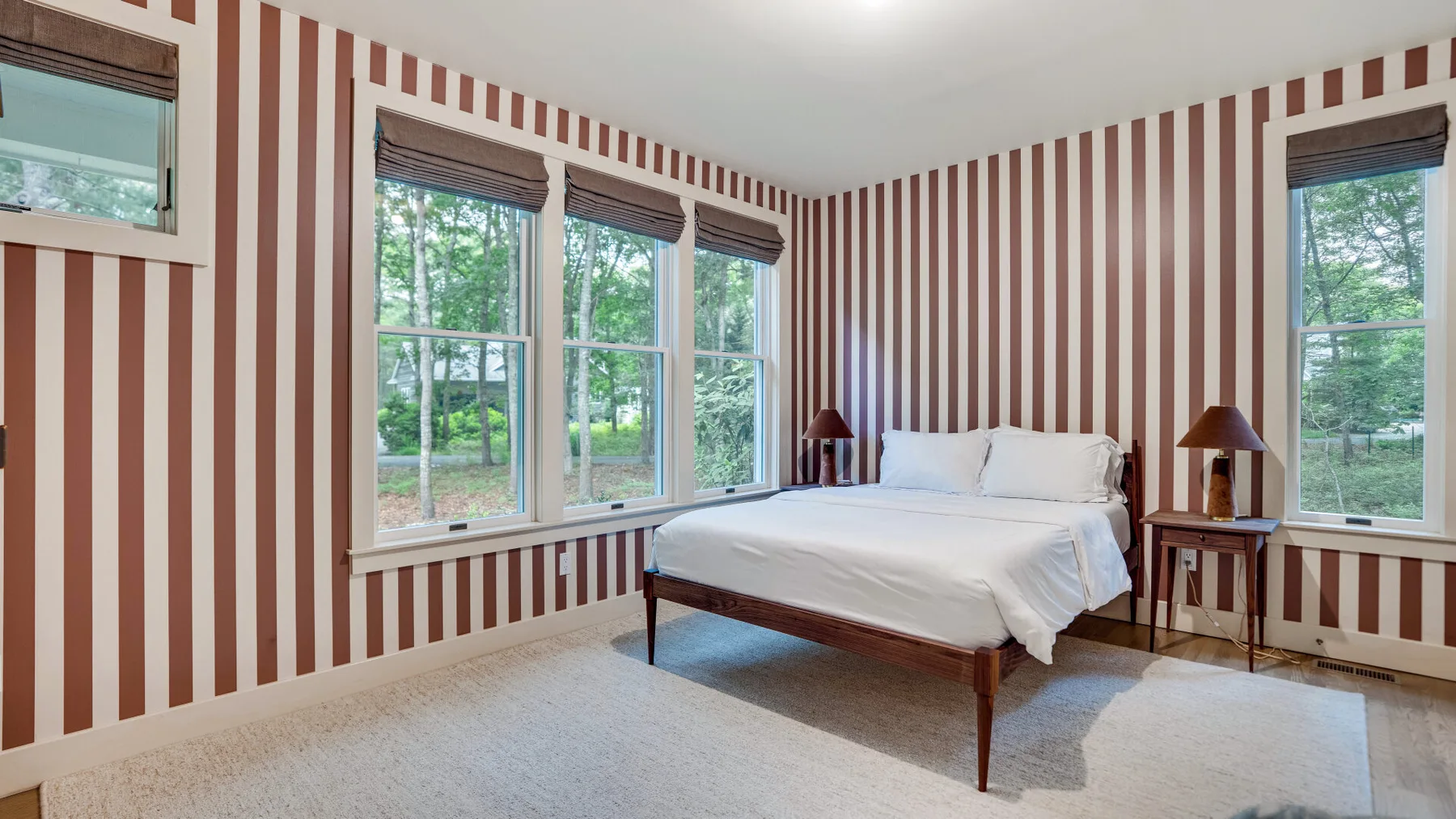 Un dormitorio con una cama, paredes a rayas y varias ventanas.
