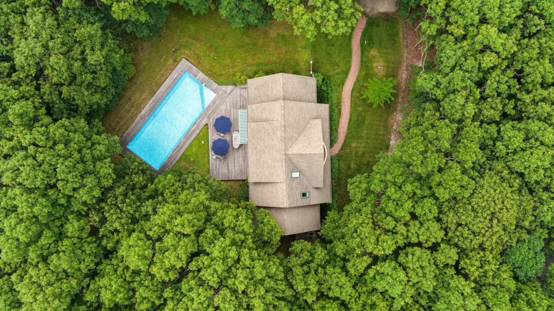 Una vista aérea muestra una casa y una piscina rodeadas de árboles frondosos.