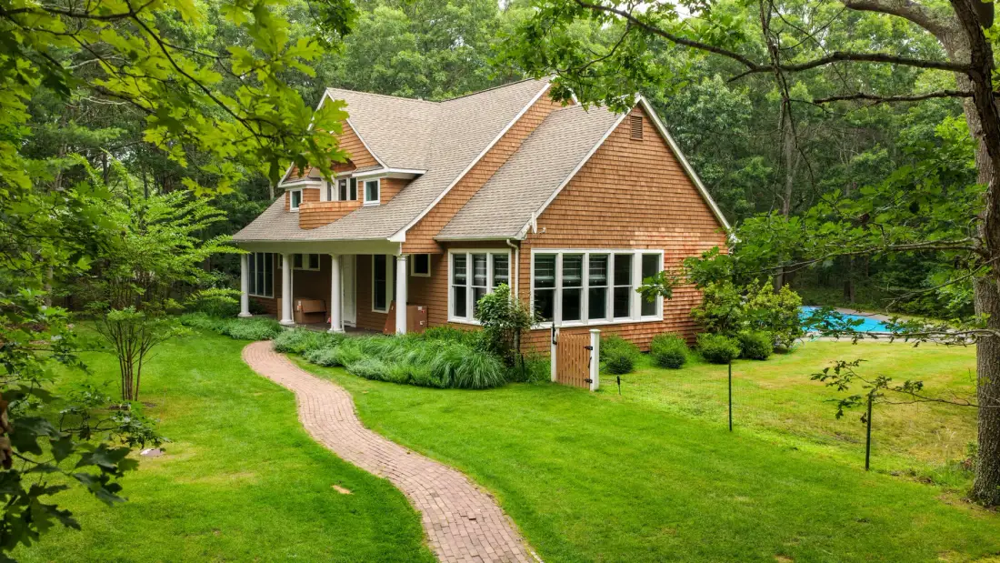 Una casa está en un jardín frondoso, con un sendero curvo que conduce a la entrada.