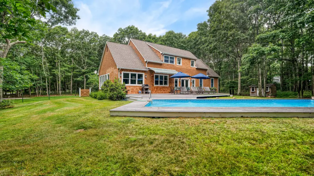 Una casa grande está junto a una piscina en un patio arbolado.