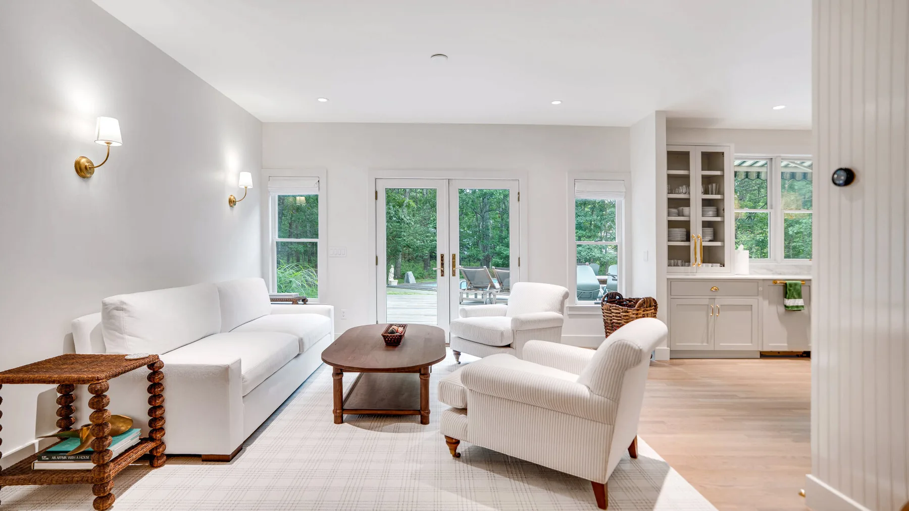 Una sala luminosa con asientos blancos, una mesa de centro y grandes ventanas.