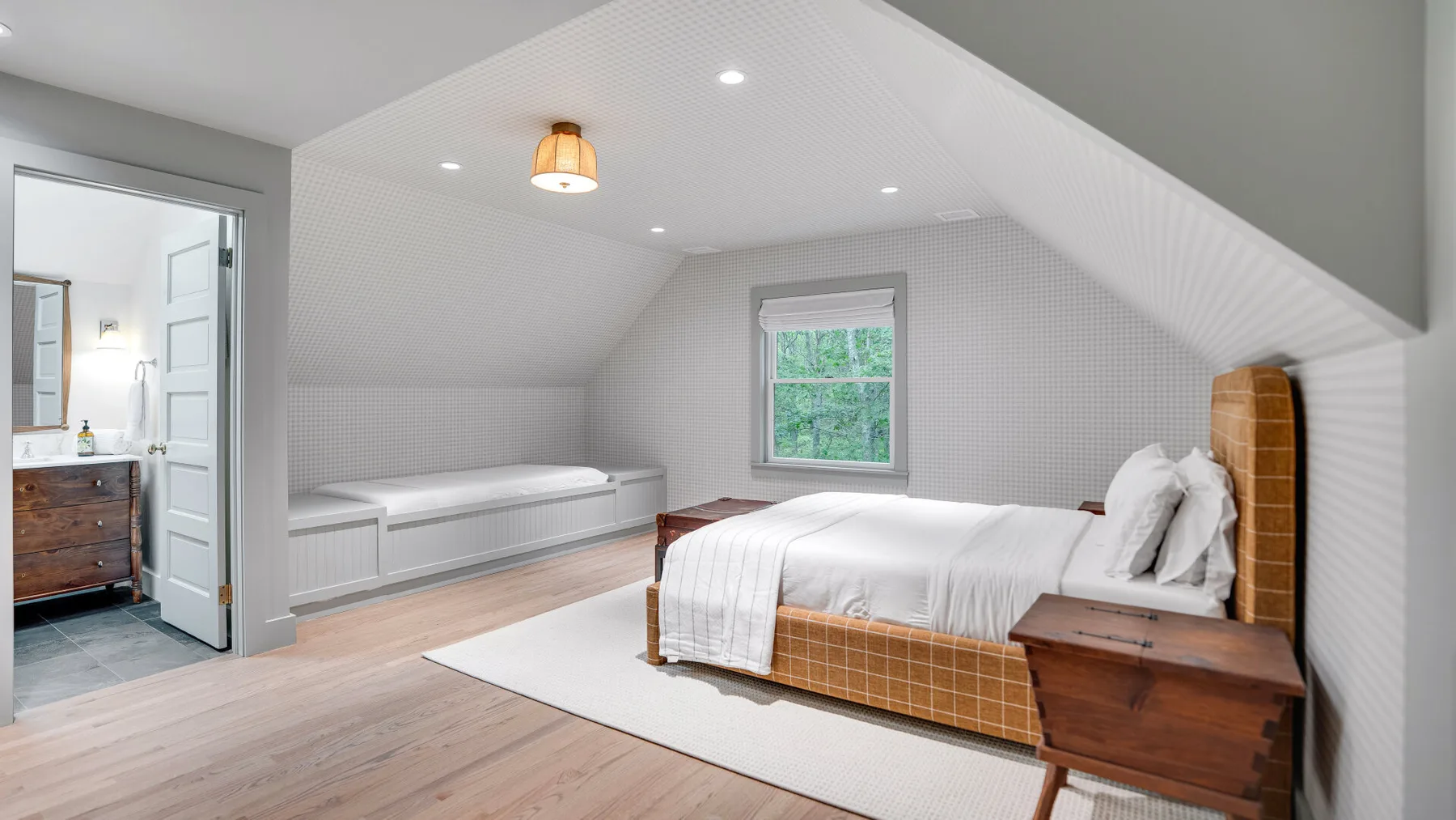 Un dormitorio abuhardillado luminoso con cama, banco empotrado y ventana.