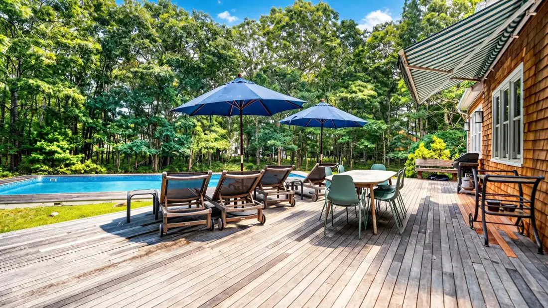 Una terraza de madera con asientos y sombrillas da a una piscina.