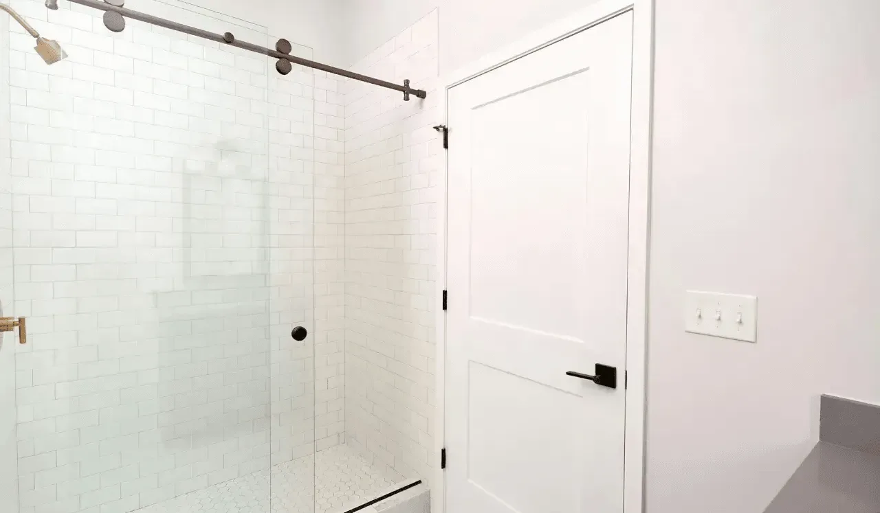 Una zona de ducha con azulejos junto a una puerta blanca.