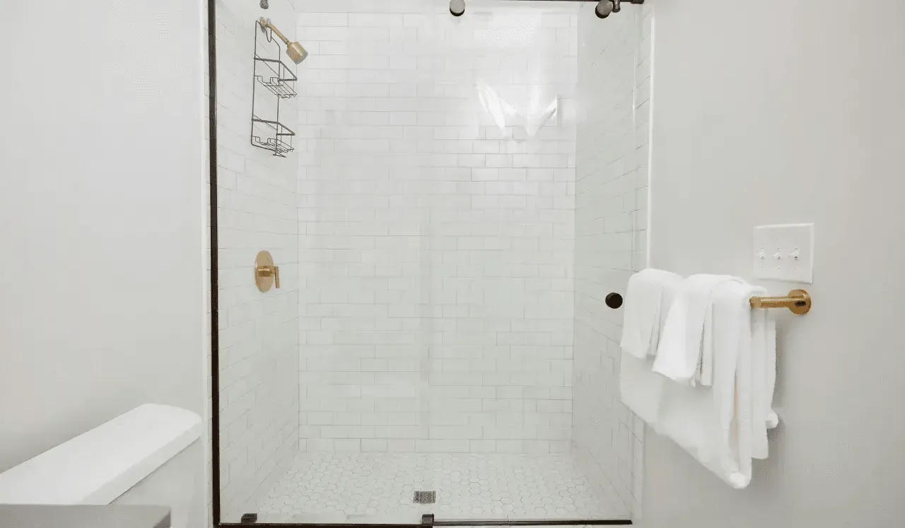Una zona de ducha con azulejos y una barra metálica con toallas blancas.