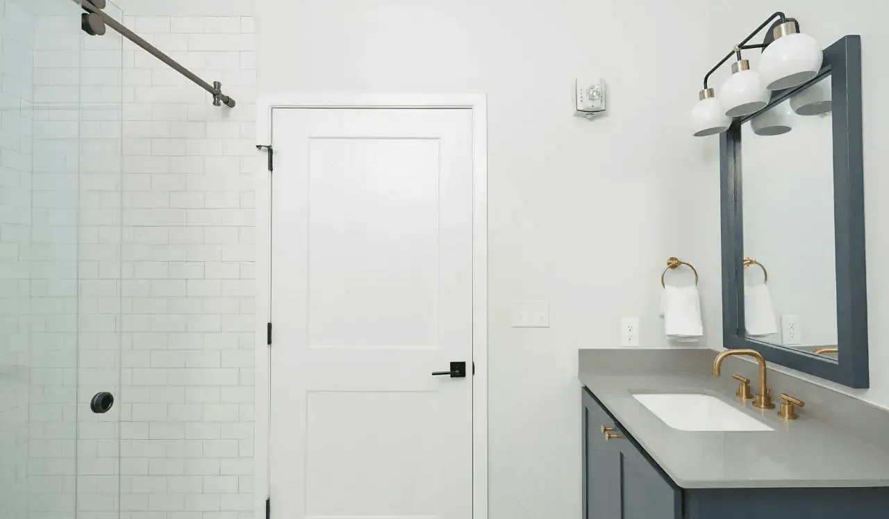 Un baño luminoso con ducha de vidrio, puerta blanca y lavabo con mueble.