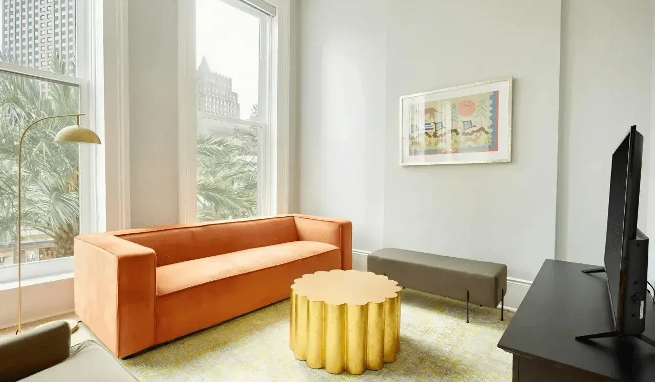 Una sala luminosa con un sofá naranja y una mesa de centro redonda dorada.