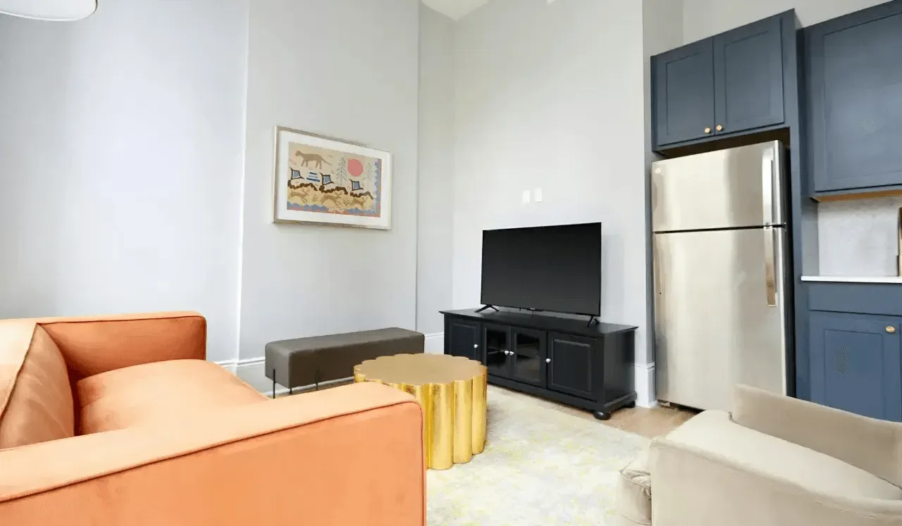 Una sala de estar con asientos, un televisor y una cocina compacta.