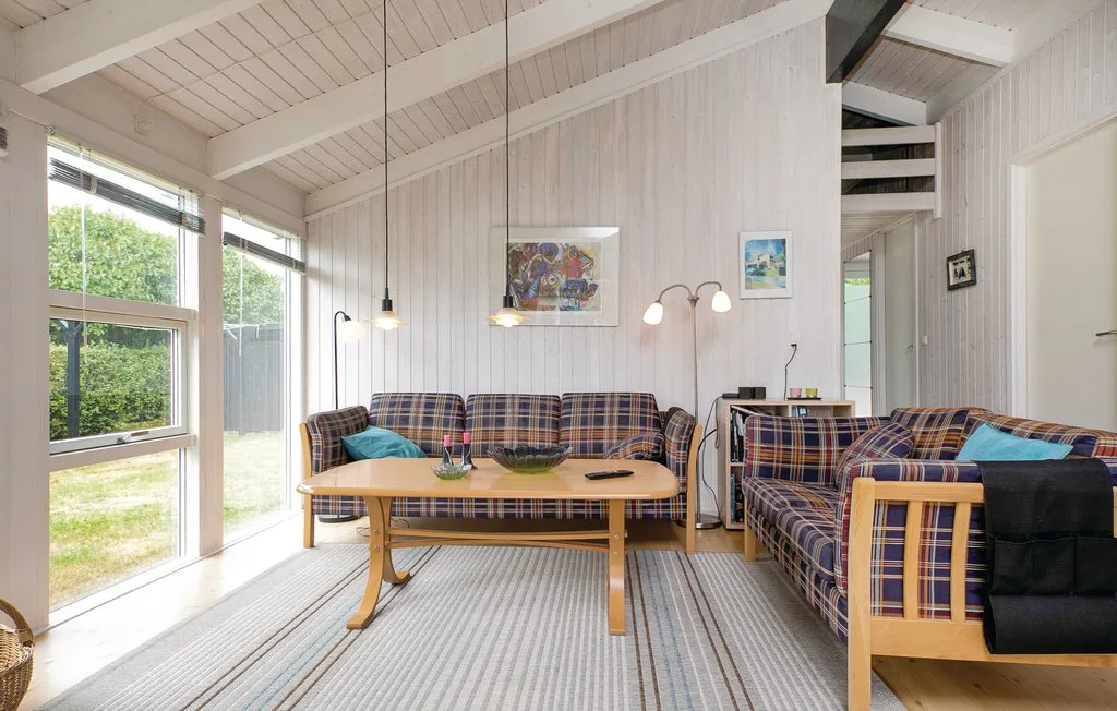 Una sala luminosa con asientos a cuadros, una mesa de centro y ventanas grandes.
