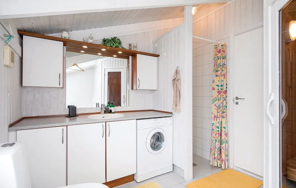 Un baño luminoso con lavabo, lavadora y zona de ducha con azulejos.
