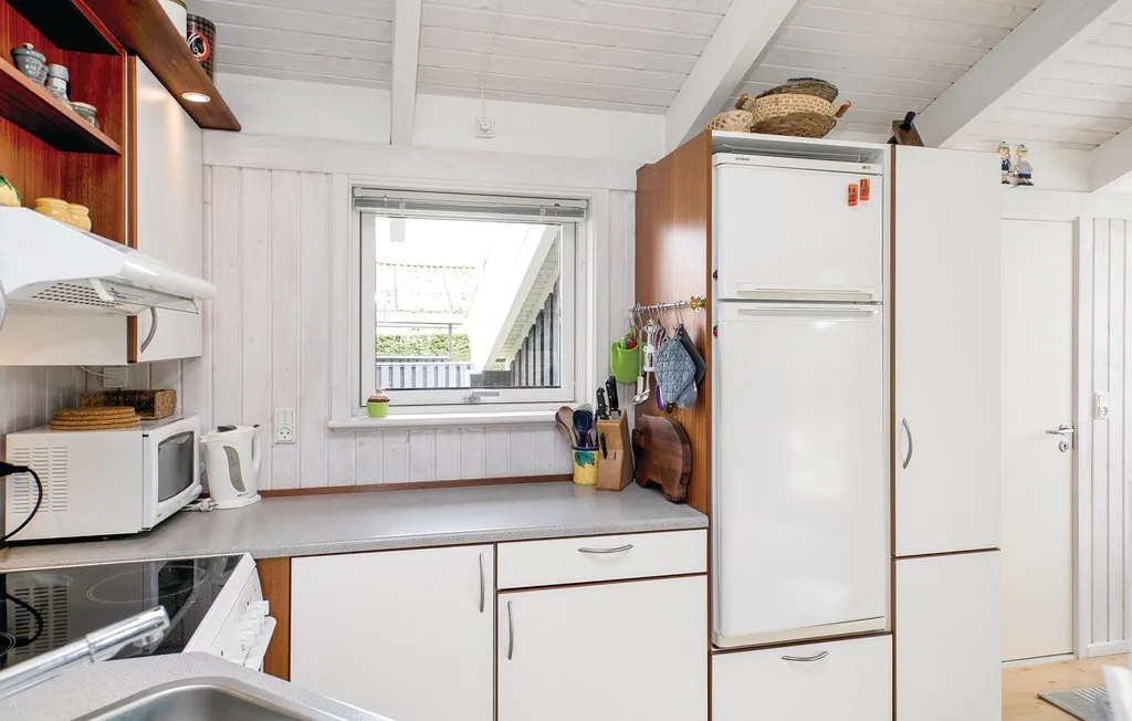 Una cocina luminosa con gabinetes blancos, un refrigerador y una ventana.