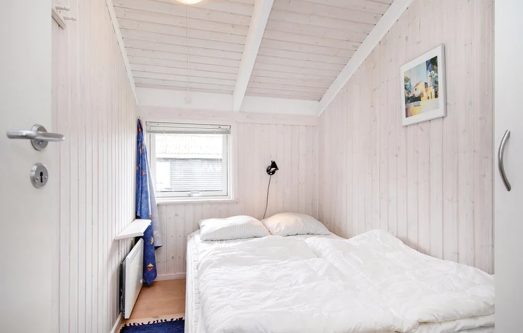 Un dormitorio pequeño con una cama bajo un techo blanco inclinado.