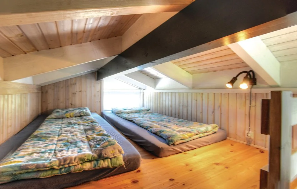 Una zona compacta para dormir con dos camas bajas bajo un techo de madera inclinado.