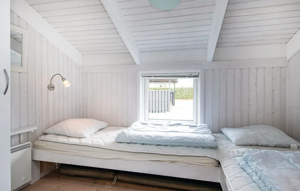 Un dormitorio compacto con una cama baja bajo un techo blanco inclinado.