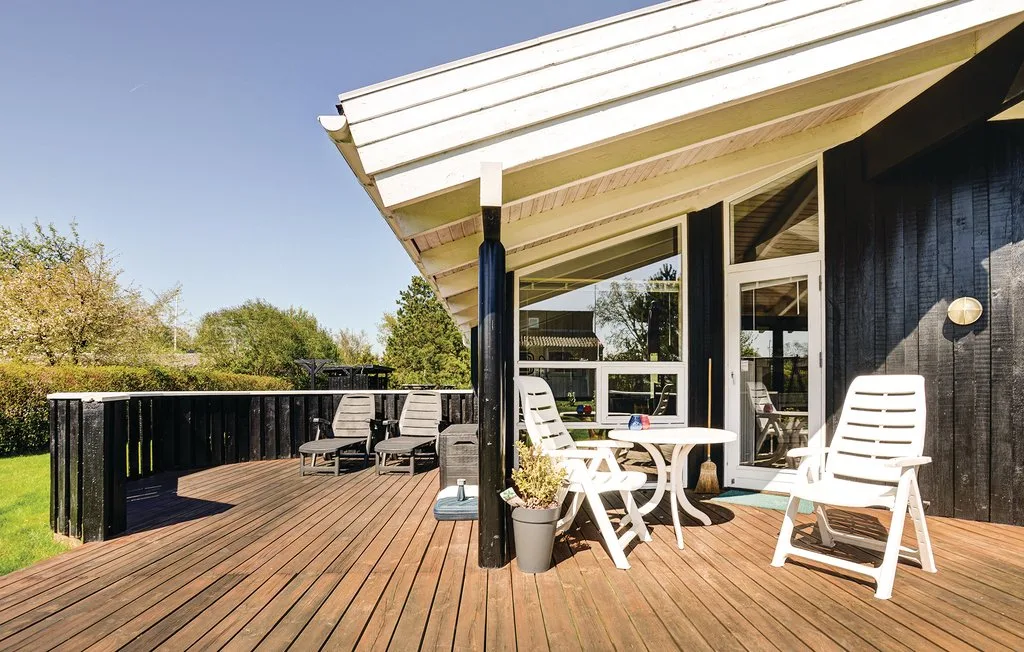 Una terraza de madera junto a una casa tiene asientos al aire libre y una mesa.