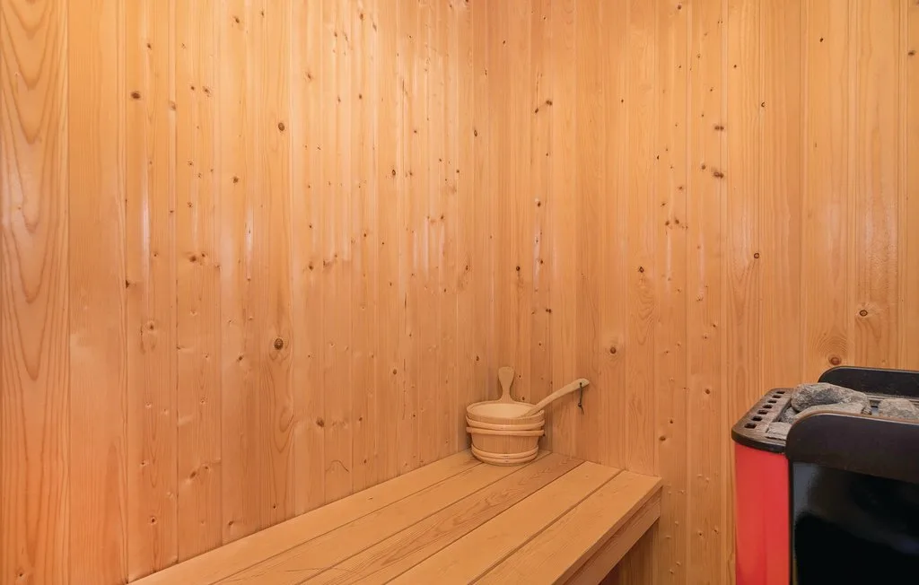 Una sauna revestida de madera con un banco largo y un cubo.