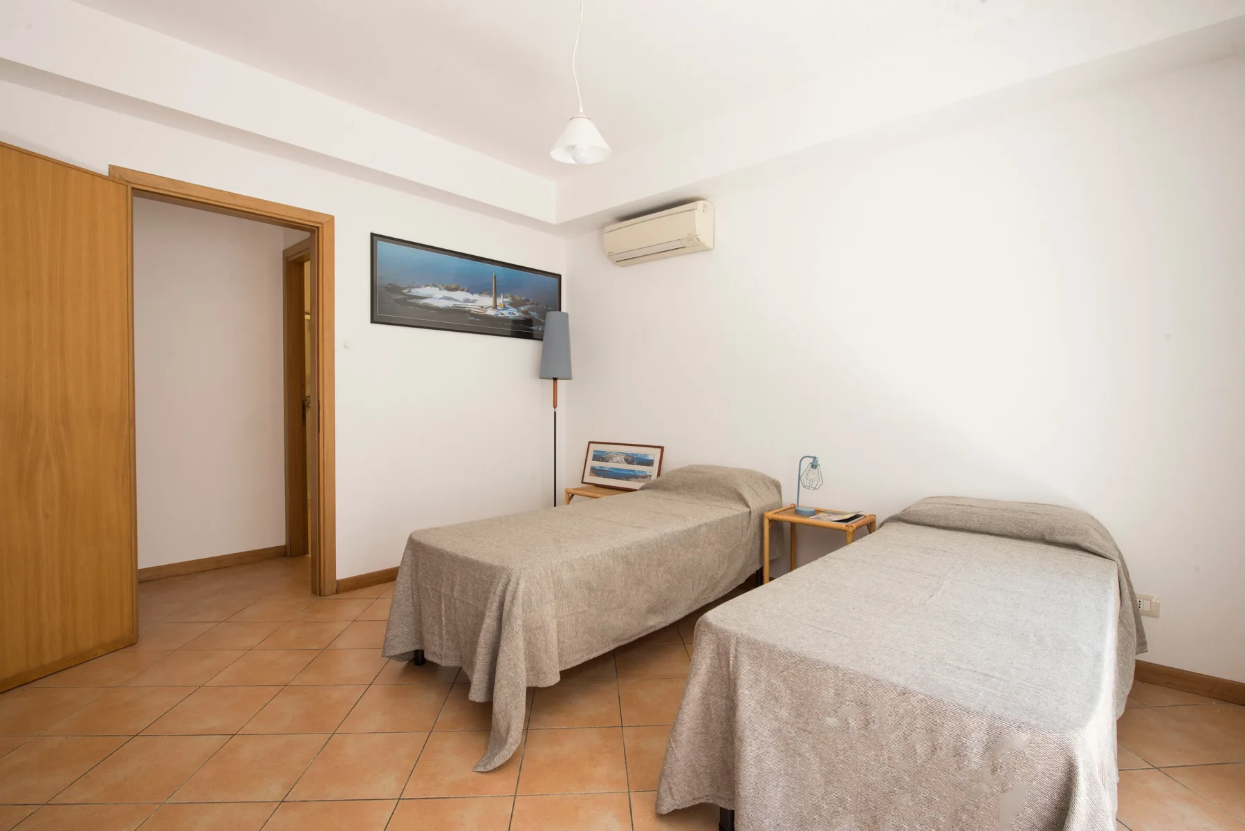 A bedroom with two single beds, a bedside table, and a wall-mounted air conditioner.