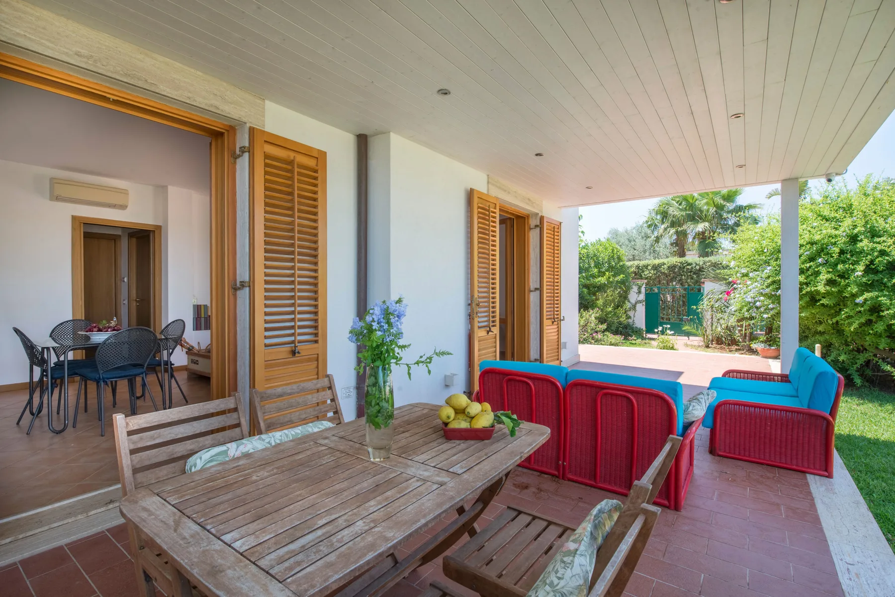 A covered patio has a wooden dining table beside a small swimming pool.