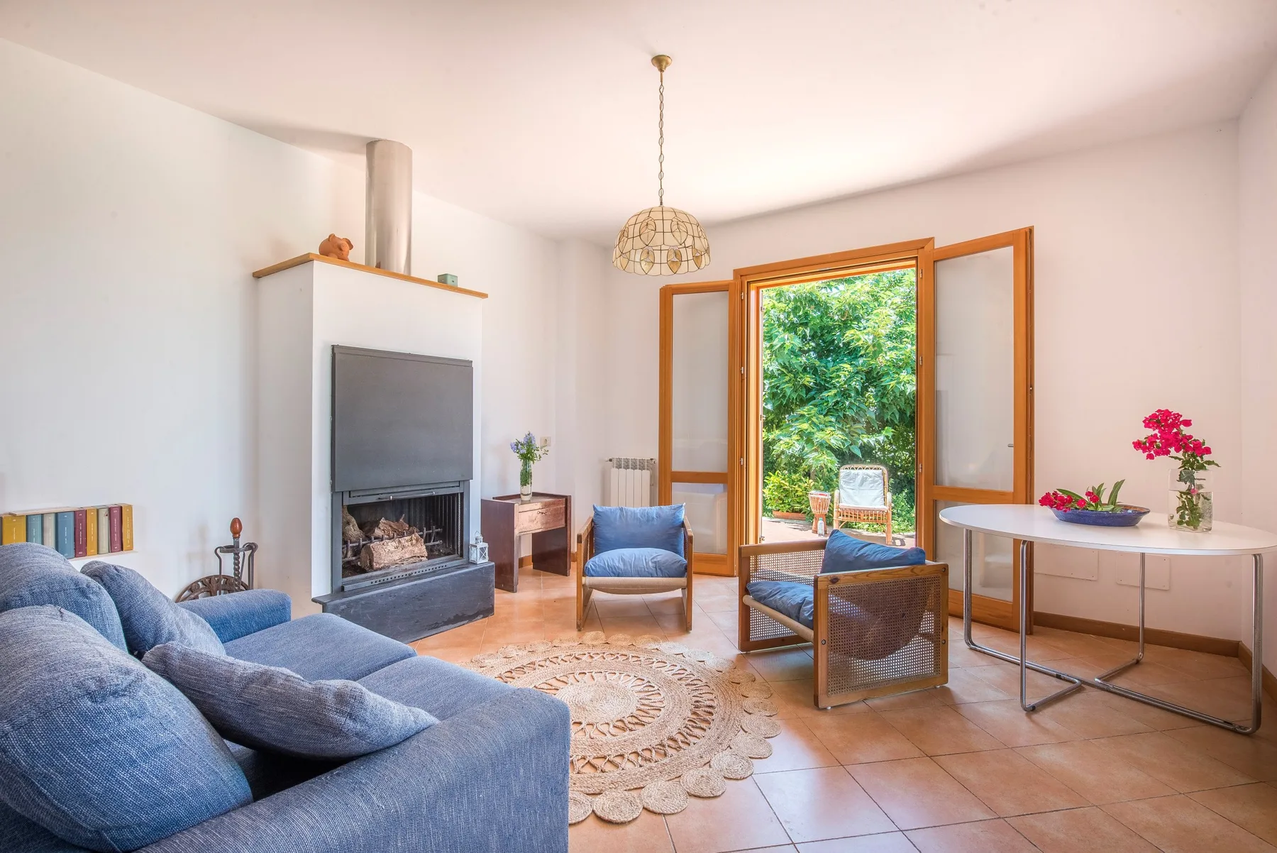 A bright living room opens through wooden doors to a leafy outdoor area.