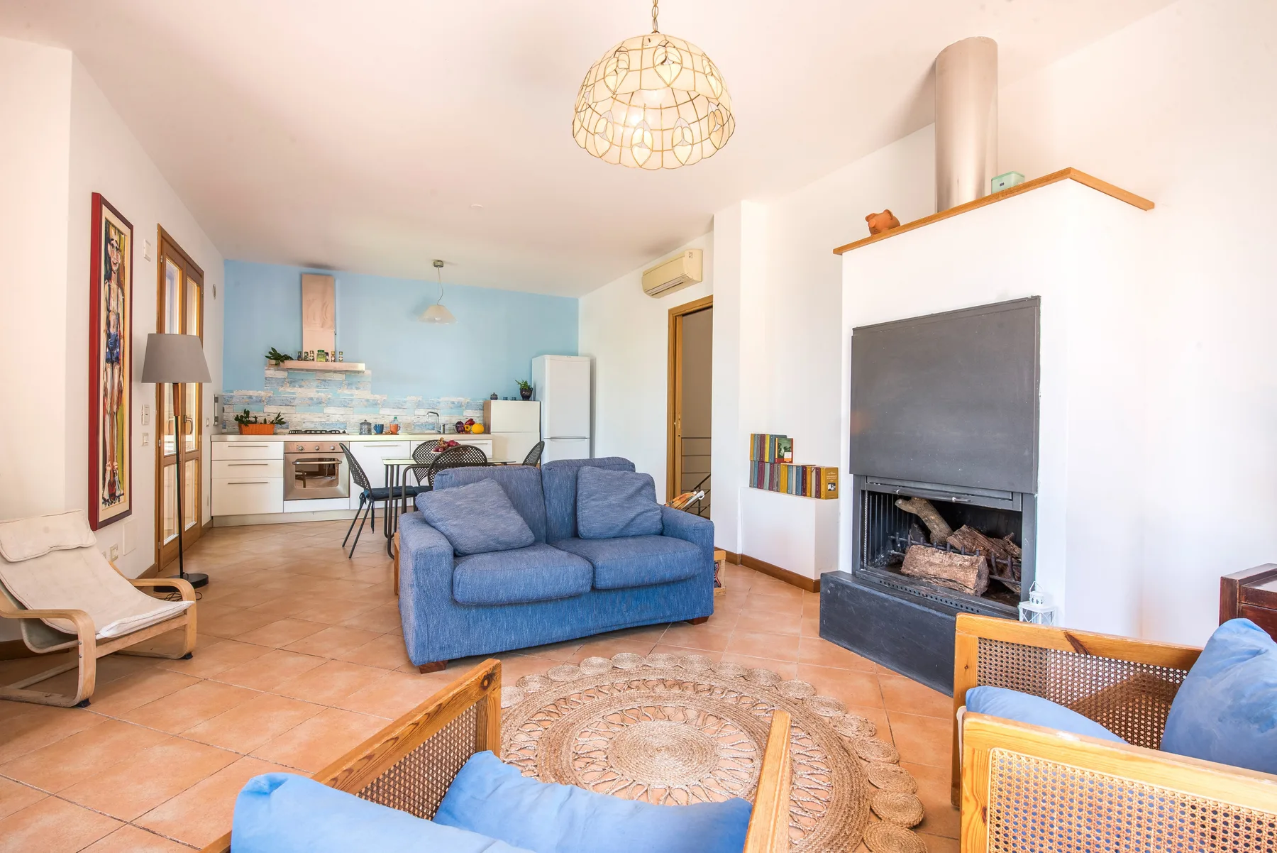 A living room with blue seating, a fireplace, and an open kitchen.