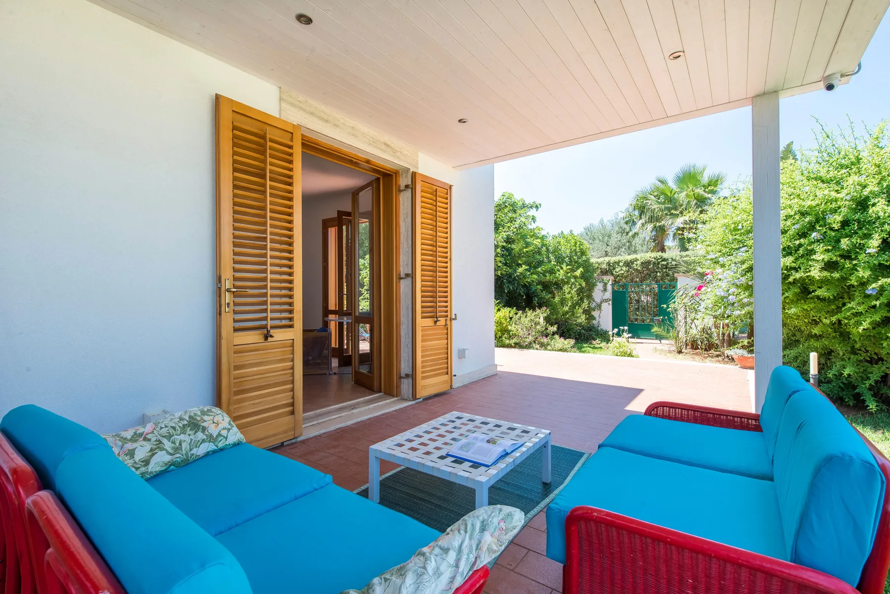 A covered patio with blue seating and an open doorway overlooking a garden.