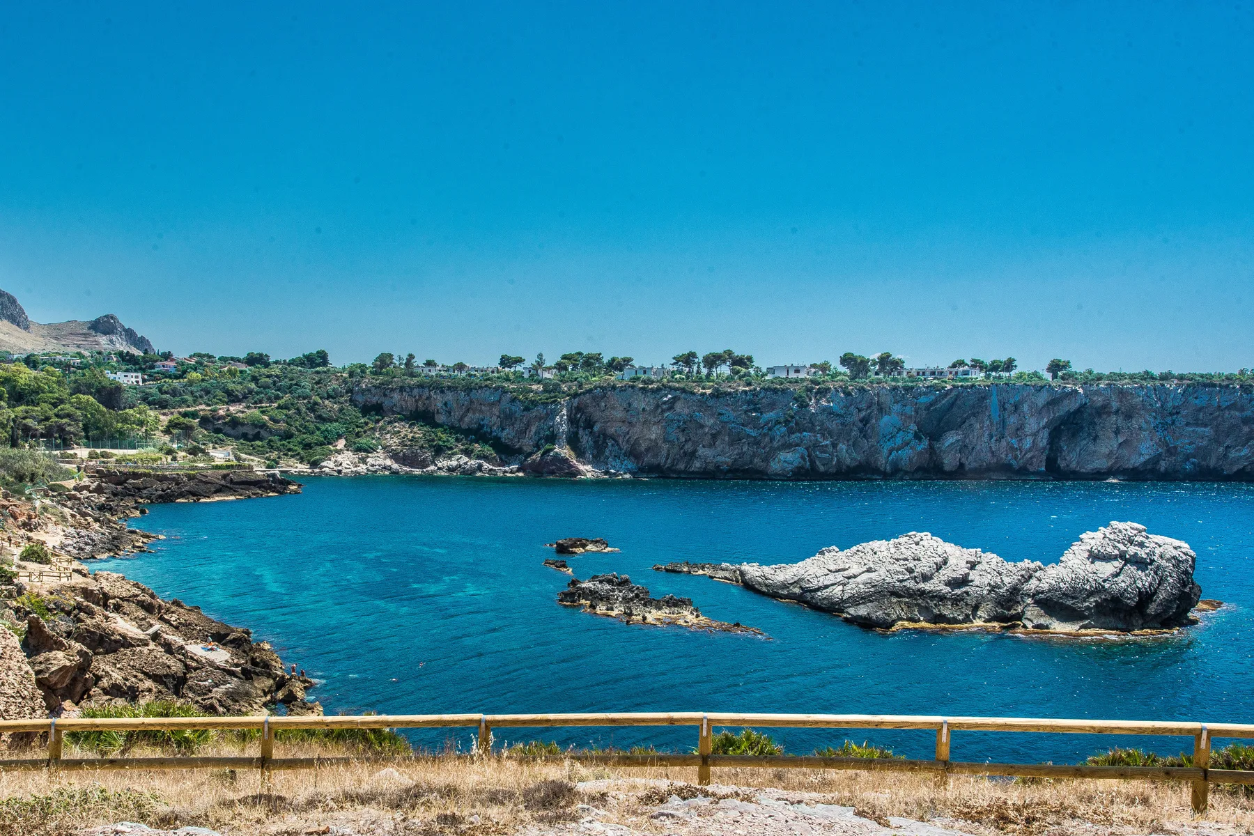 A coastal inlet with blue water, rocky cliffs, and a dry grassy foreground.